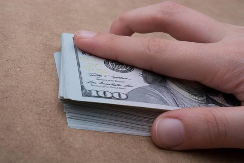 Hand holding banknote bundle of US dollar on a linen canvas background