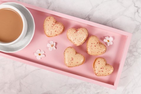 Heart shaped French macaron sweets on pink tablet with coffee cup