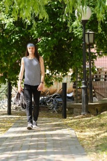 Young man with long hair in tank top and jeans walks along sidewalk