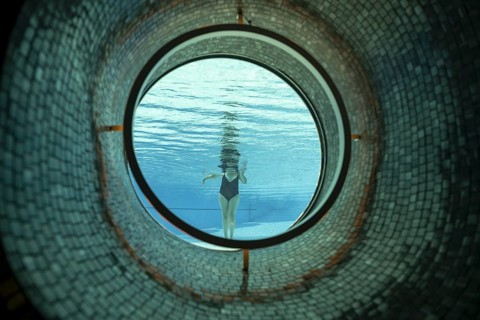 Woman Standing in the Ship Porthole in Underwater in Swimming Pool in a Sunny Day in Switzerland