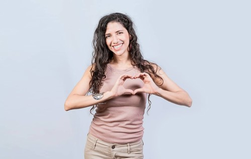 Smiling young woman making heart shape with her hands. Teen girl making heart shape with her hands