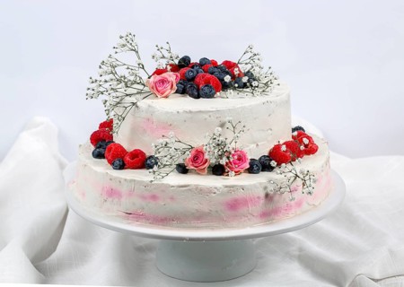 A two tier wedding cake decorated with berries and flowers festive cream cake on a light background