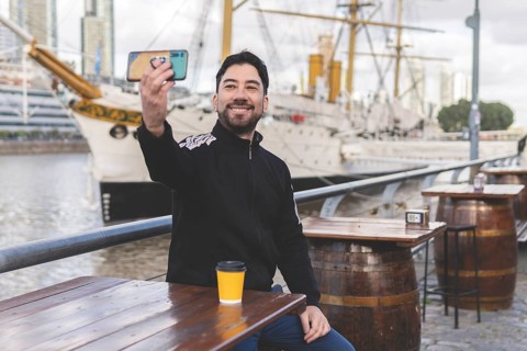 Latin tourist drinking coffee and taking a selfie at an outdoor bar in Puerto Madero