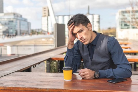 Businessman sitting in an outdoor bar having a coffee clutching his head with a worried expression