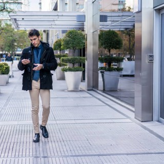 A serious businessman reading a message on his smartphone while walking in the street near his office