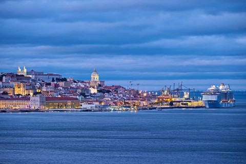 View of Lisbon over Tagus river with passing ferry boat from Almada with moored cruise liner in evening twilight. Lisbon
