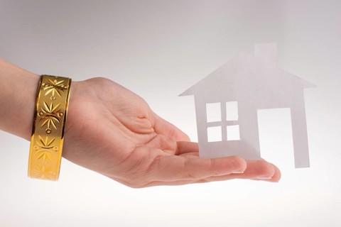 Hand holding a paper house with a golden bracelet