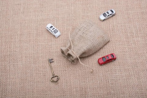 Key and toy cars around a sack on a linen canvas