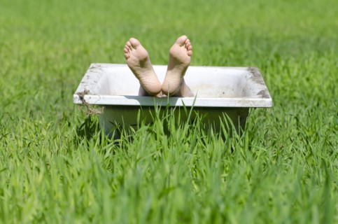 Woman lying in a bathtub on a green field