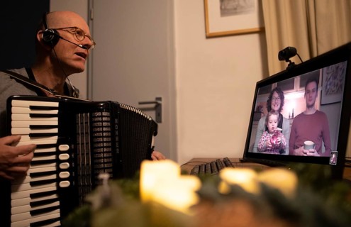 Christmas in times of great distance. Grandfather with accordion in front of a screen showing his family.
