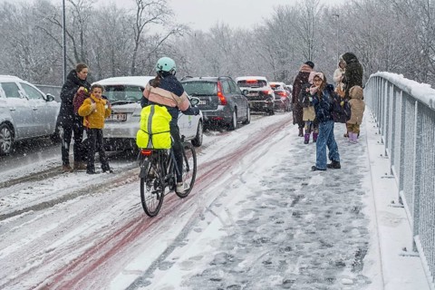 Cyclist and children walking to school over slippery pavement on bridge covered in sleet during unexpected late snow shower in March