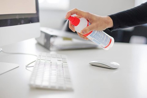 Hygiene at the workplace. A woman disinfects the keyboard at her workplace with disinfectant spray. Berlin