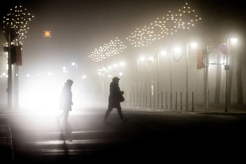 Two people walk along a street decorated with Christmas lights in the fog in Niesky