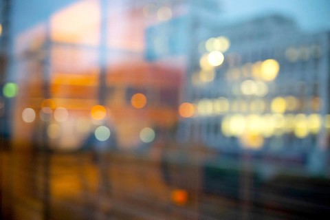 Daydream photographed from the window of a train. Blurred image with lights of a city and the reflection of a train compartment