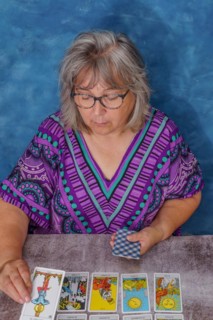 Older woman with white hair and glasses casting tarot cards