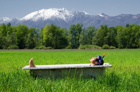 Woman lying in a bathtub on a green field with grass and trees
