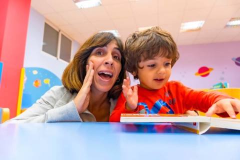 Woman teacher with a child sitting at a table reading a story book