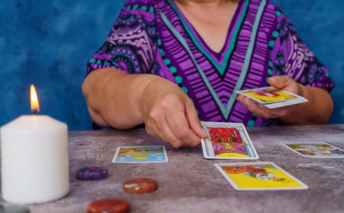 Unrecognizable woman casting tarot cards on the table candles and chakra stones