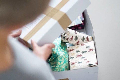 Symbolic photo on the subject of sending Christmas presents by post. A woman opens a parcel with Christmas presents. Berlin