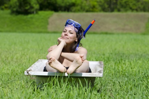 Woman Sitting in a Bathtub on a Green Field with Grass and a Diving Mask in a Sunny Day