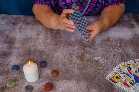 Woman shuffling tarot cards on a table with candles and chakra stones
