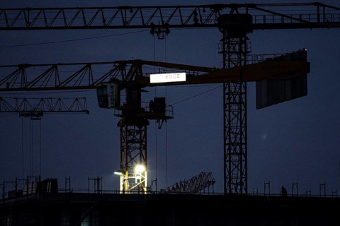 A worker draws on scaffolding and in front of a crane on a newly built house