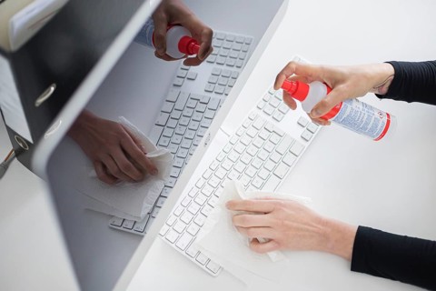 Hygiene at the workplace. A woman disinfects the keyboard at her workplace with disinfectant spray. Berlin