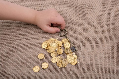 Hand holding a retro styled key over fake gold coins