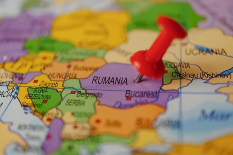 Romania marked with a red thumbtack on a map with an out-of-focus background