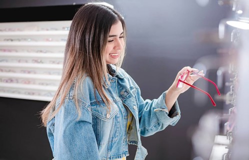 Customer choosing glasses in an eyewear store. Beautiful girl choosing glasses in an optical store