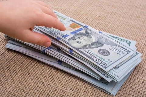 Toddler hand holding banknote bundle of US dollar on a linen canvas background