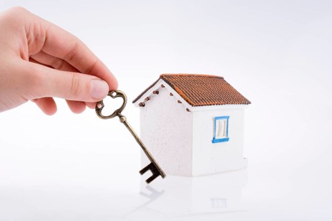 Hand holding a golden key near a house on a white background