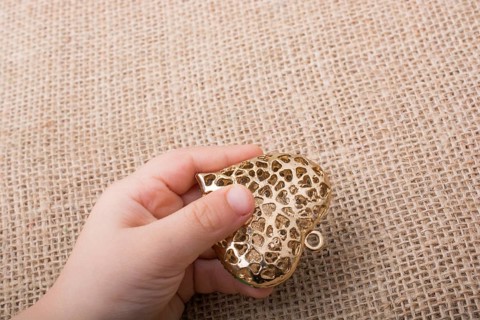 Heart shaped gold color metal object in hand