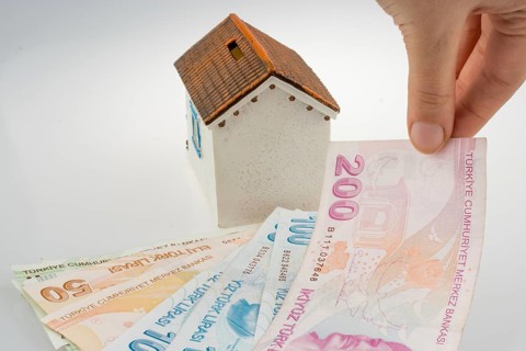 Hand holding Turkish Lira banknotes by the side of a model house on white background