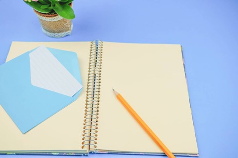 Pencil on a blank notebook with a blue envelope with a letter in it