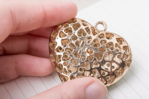 Heart shaped gold color metal object in hand