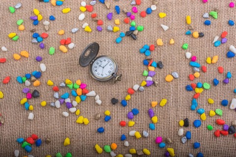 Pocket watch amid colorful pebbles on canvas background