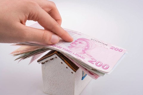 Hand holding Turkish Lira banknotes on the roof of a model house on white background