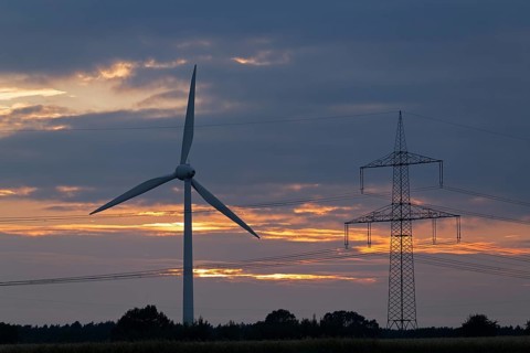 Wind power station and high voltage pylon in front of evening sky