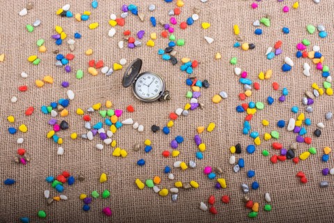 Pocket watch amid colorful pebbles on canvas background