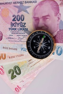 Turkish Lira banknotes by the side of a compass on white background