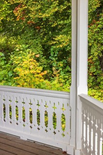 Railing on a porch with white wooden carpentry by a deciduous trees in autumn colors