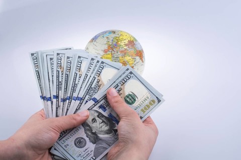 Human hand holding American dollar banknotes by the side of a model globe on white background