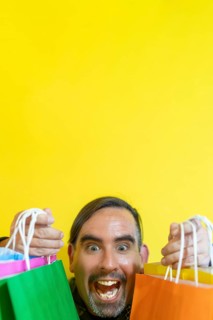 Happy smiling man holding shopping bags on yellow background. Joy of consumption. Purchases