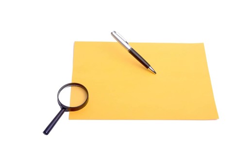 Pen and magnifying glass placed on yellow paper