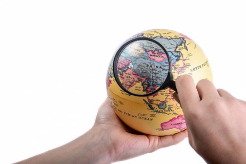 Hand holding a magnifying glass on globe in hand on white background