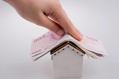 Hand holding Turkish Lira banknotes on the roof of a model house on white background