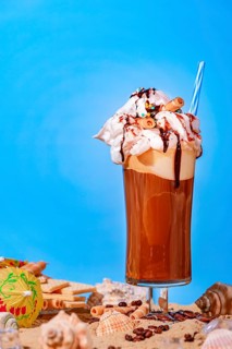 Iced coffee with whipped cream and chocolate sauce on sand