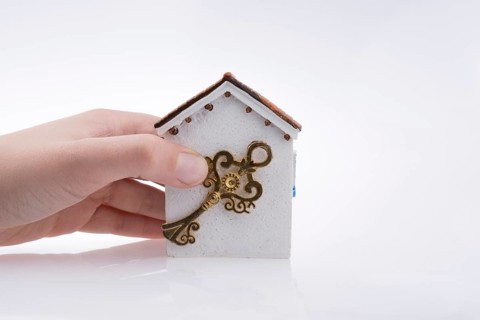 Hand holding a golden key near a house on a white background
