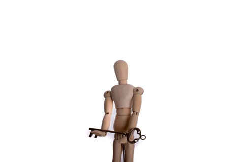 Puppet holding an antique golden key in hand on a white background